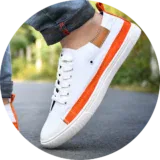White canvas shoes for men - stylish and comfortable sneakers for casual wear. A close-up of a stylish men's sneaker in white with orange accents, worn with rolled-up denim jeans on an outdoor road.