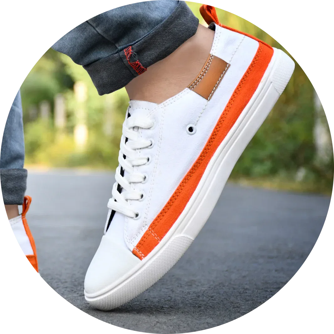 White canvas shoes for men - stylish and comfortable sneakers for casual wear. A close-up of a stylish men's sneaker in white with orange accents, worn with rolled-up denim jeans on an outdoor road.