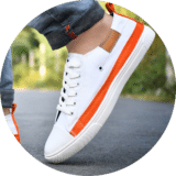 White canvas shoes for men - stylish and comfortable sneakers for casual wear. A close-up of a stylish men's sneaker in white with orange accents, worn with rolled-up denim jeans on an outdoor road.