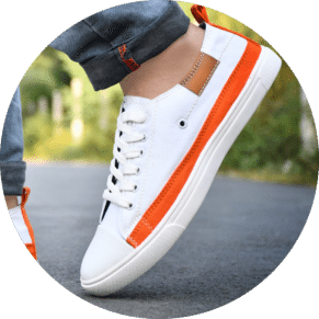 White canvas shoes for men - stylish and comfortable sneakers for casual wear. A close-up of a stylish men's sneaker in white with orange accents, worn with rolled-up denim jeans on an outdoor road.
